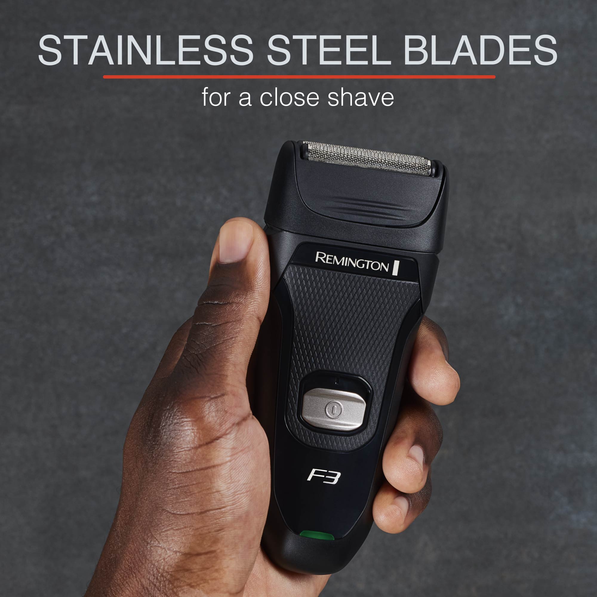 Hand holding a Remington electric shaver with text about stainless steel blades on a dark background
