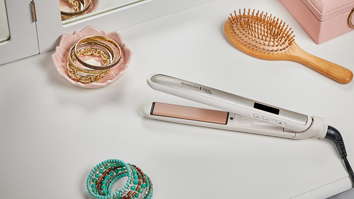 Hair straightener on a table with hairbrush, hair accessories, and jewelry