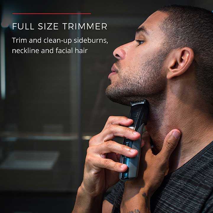 Man using a full-size trimmer to trim sideburns, neckline, and facial hair in a bathroom setting.