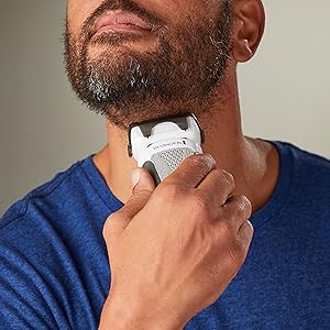 Man using an electric razor on his beard against a neutral background
