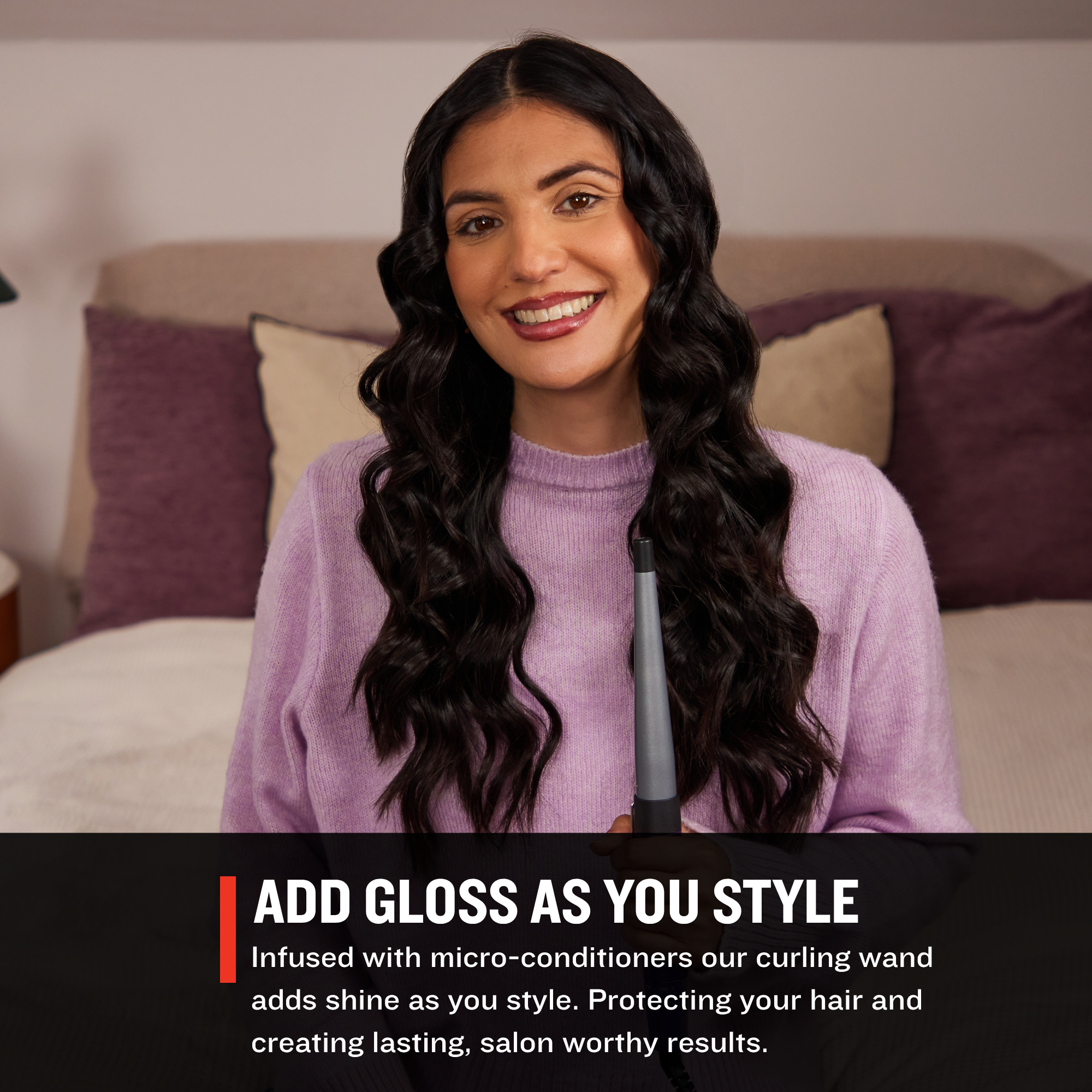 Woman with styled hair holding a curling wand in a bedroom setting