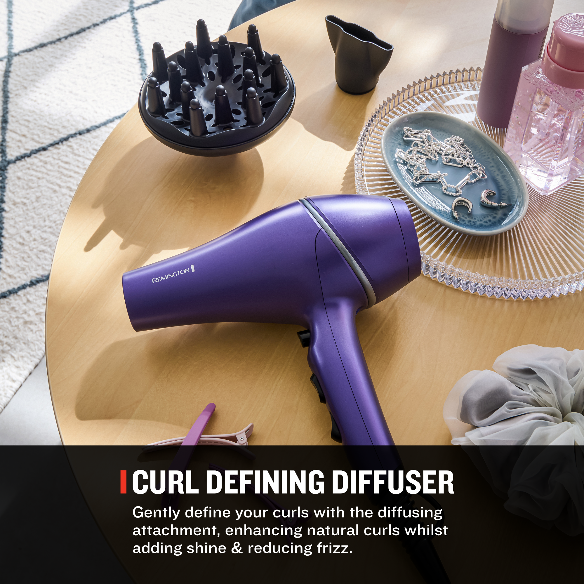 A purple Remington hair dryer with a black curl defining diffuser attachment, styled on a light wood table with beauty accessories. A black text banner at the bottom reads 'CURL DEFINING DIFFUSER' with descriptive text.