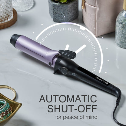A Remington curling iron with a metallic lavender-purple barrel and black handle, placed on a light marble surface with decorative lifestyle props around it. White text at the bottom reads 'AUTOMATIC SHUT-OFF for peace of mind' with a clock graphic behind the iron.