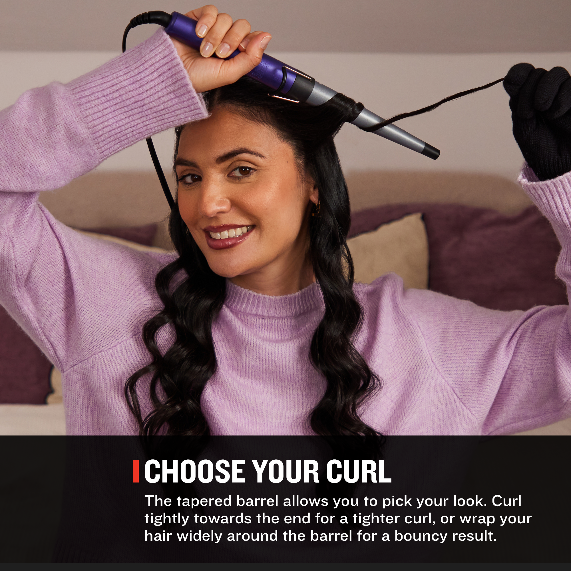 A woman with long dark wavy hair uses a purple and silver curling iron on her hair in a bedroom setting. A black text banner at the bottom reads 'CHOOSE YOUR CURL' with descriptive text about curling hair.