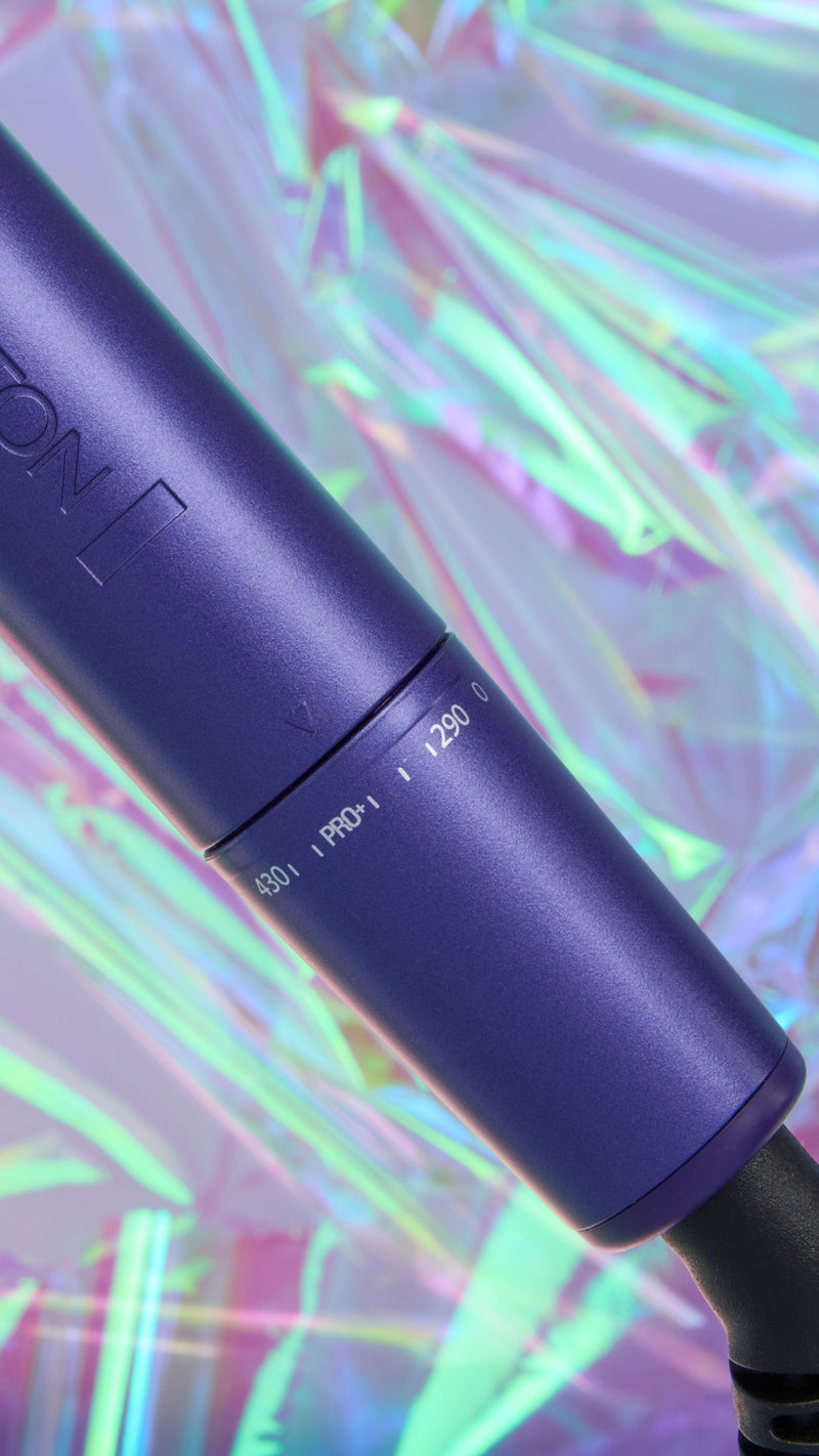 A close-up of a purple hair curling wand barrel with white printed settings, set against a vibrant, iridescent holographic background.