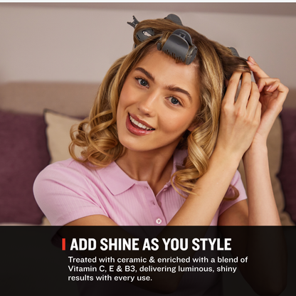 A woman with styled wavy hair wearing a pink polo shirt sits indoors, demonstrating the use of Remington heated rollers. Text at the bottom reads 'ADD SHINE AS YOU STYLE' with additional descriptive copy about treating hair with Vitamin C, E, and B3.