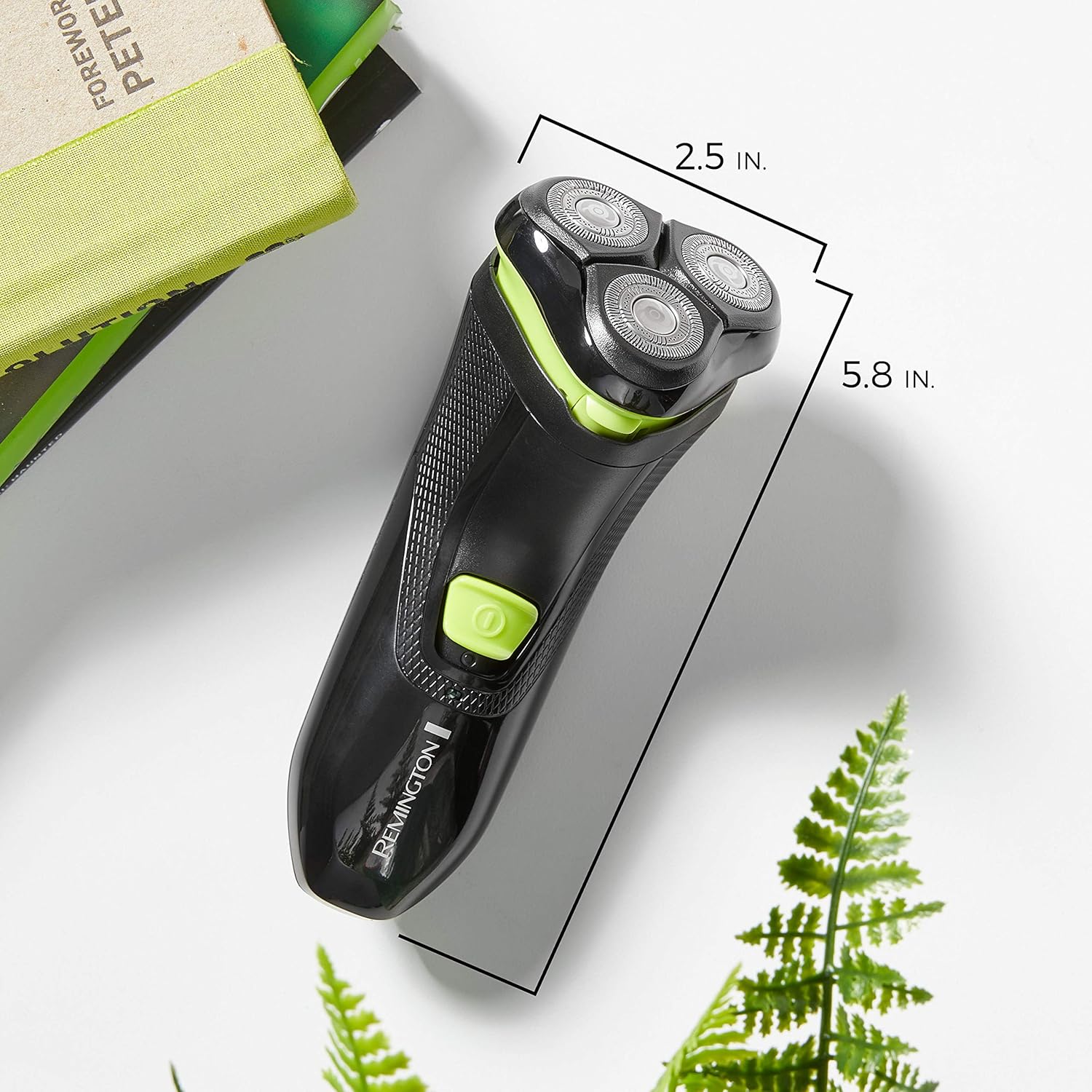 Black and green electric shaver with measurements on a light background